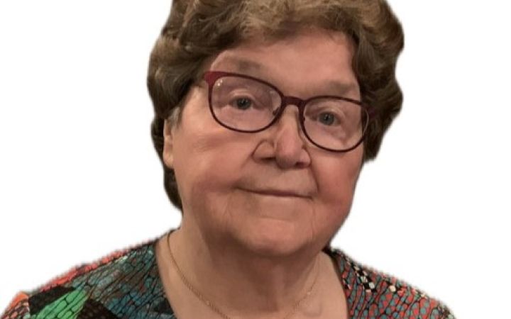 Lähikuva hymyilevästä naisesta, jolla on lyhyet hiukset ja punaiset silmälasit.