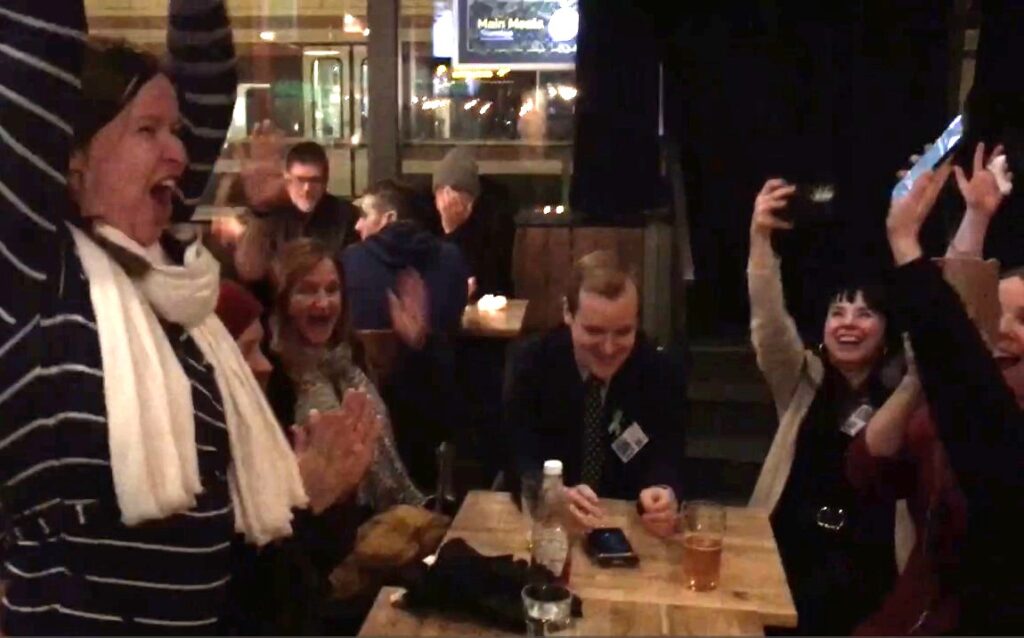 Riemuitsevia ihmisiä kädet ylhäällä baaripöydän ympärillä
