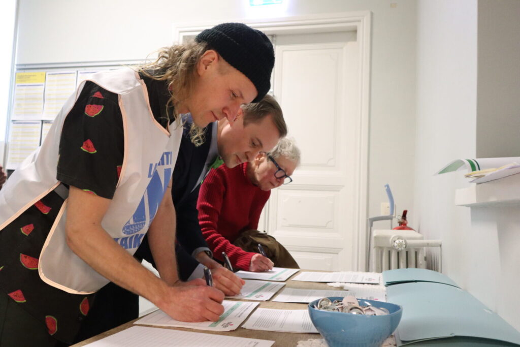Kolme ihmistä ovat kumartuneet pöydän ylle allekirjoittamaan manifestin.