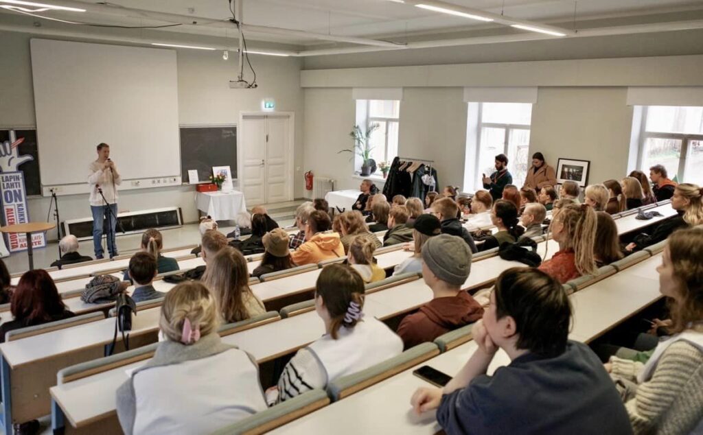 Kuva auditorion takapenkiltä kohti lavaa. Auditorio täynnä kuulijoita. Ville Merinen luennoi auditorion etuosassa.