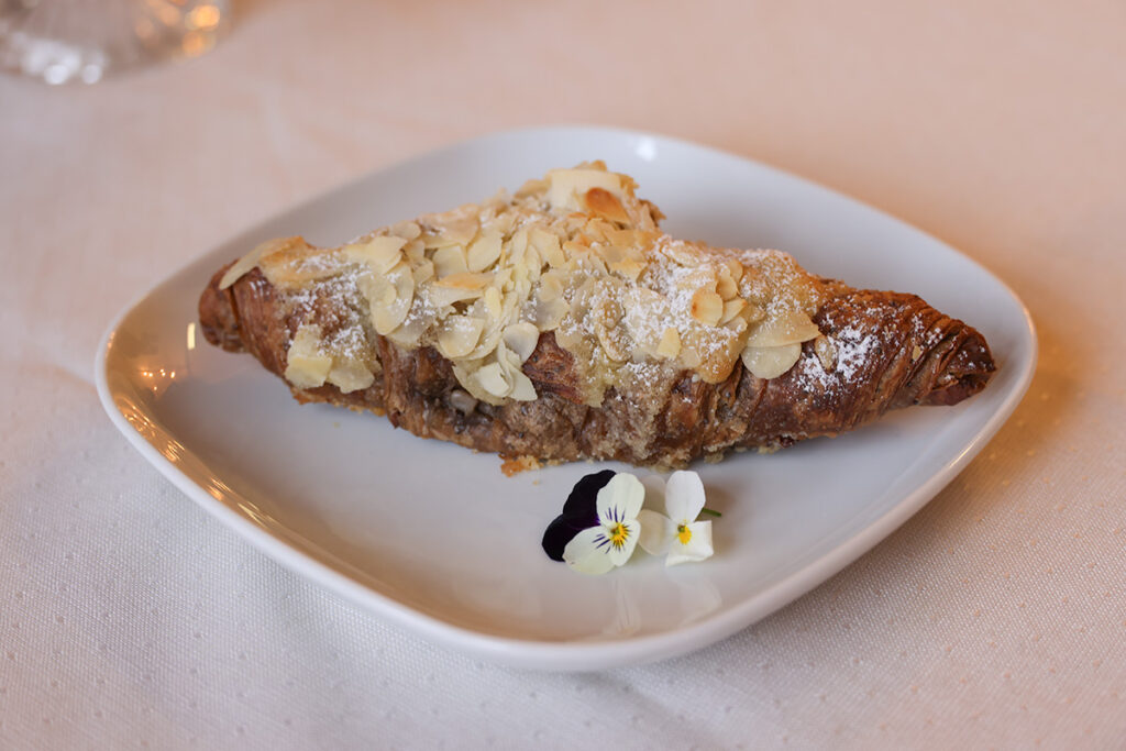 Kuvassa mantelicroissant, jonka pinnalla tomusokeria ja mantelilastuja.