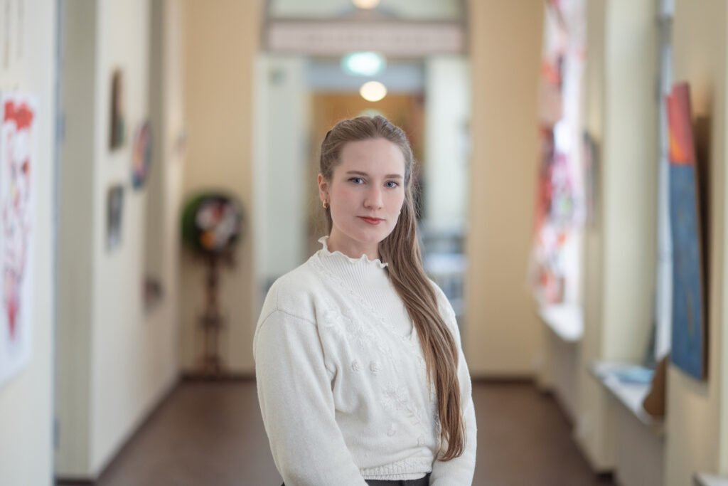 Karolina seisoo valoisalla käytävällä.