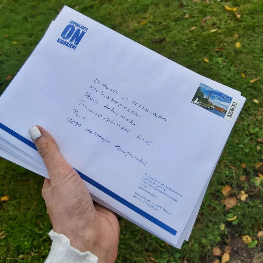 Käsi pitelemässä kirjekuorinippua. Taustalla näkyy nurmikkoa