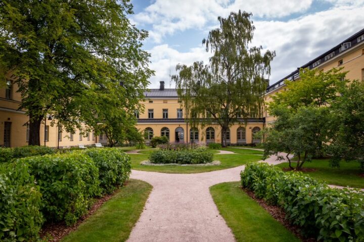 Kesäisen vehreä muotopuutarha ja päärakennuksen keltainen ulkoseinä
