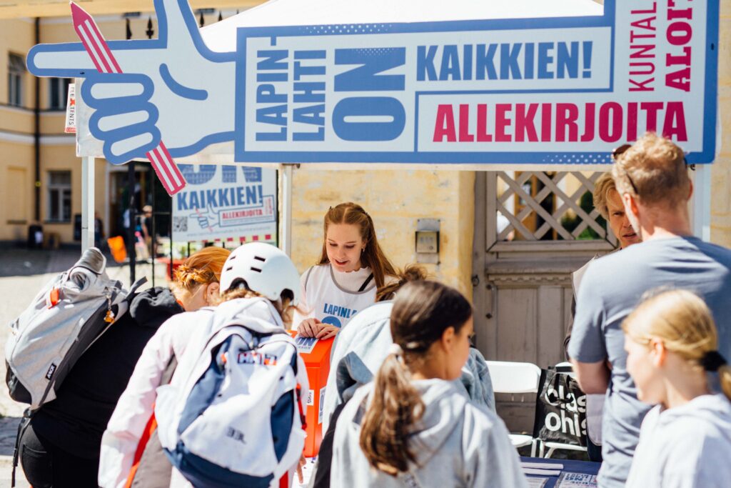 Aurinkoinen kuva kampanjateltasta, jonka edustalle on kerääntynyt ihmisiä